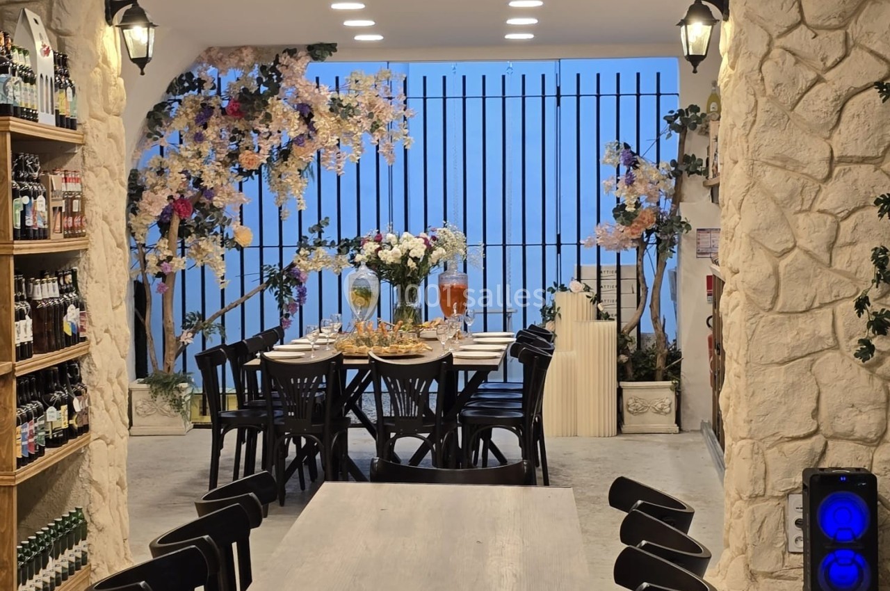 Salle à manger décorée avec des fleurs, tables en bois, chaises noires et étagères de bouteilles sur le côté.