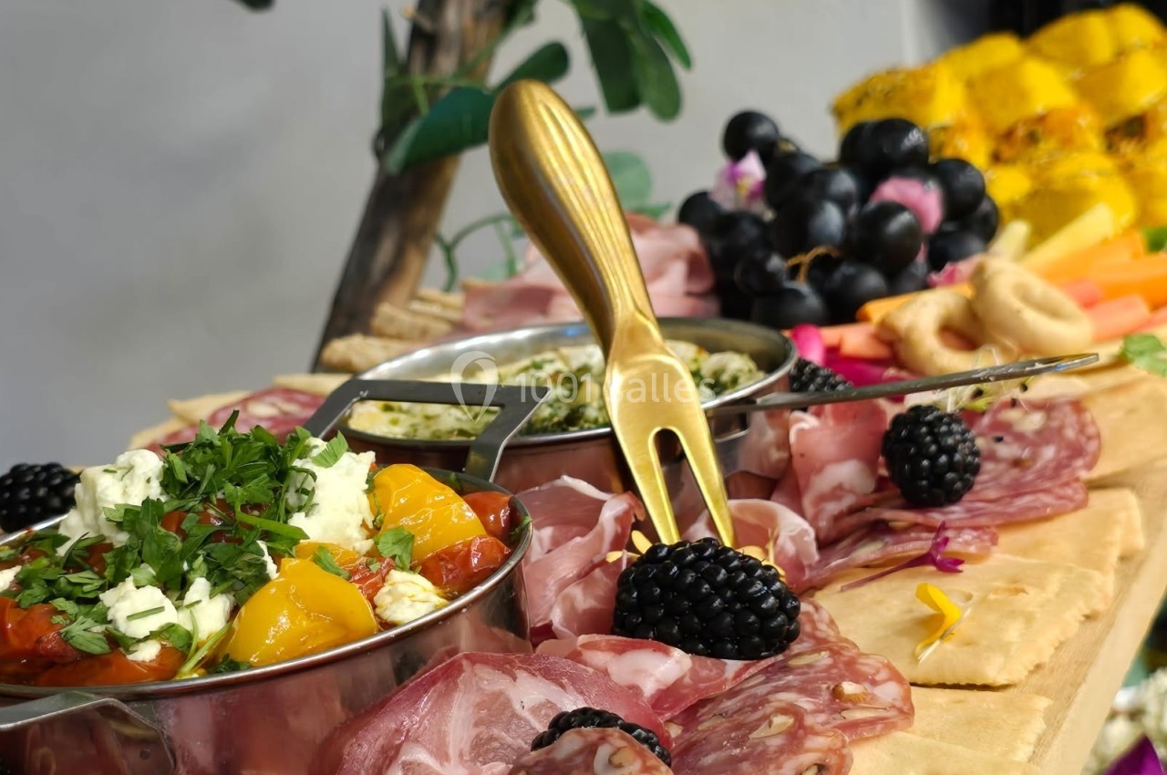 Plateau de charcuterie avec salami, légumes marinés, mûres, pain plat et décorations végétales.