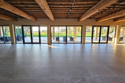 Salle spacieuse avec parquet en bois, poutres apparentes et tables disposées en U entourées de chaises noires.