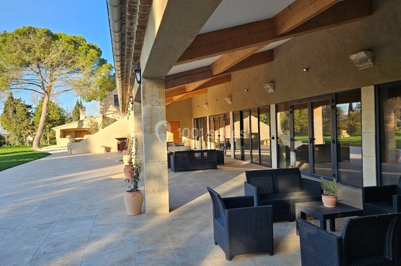Terrasse spacieuse avec mobilier de jardin en rotin, donnant sur un espace vert et une façade vitrée.