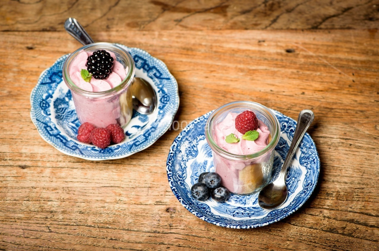 Deux verrines de mousse rose garnies de fruits rouges et feuilles de menthe, posées sur des assiettes en porcelaine bleue.