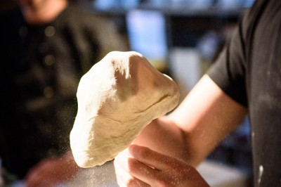 Une personne manipule une pâte à pizza en la faisant tourner dans un environnement de cuisine.