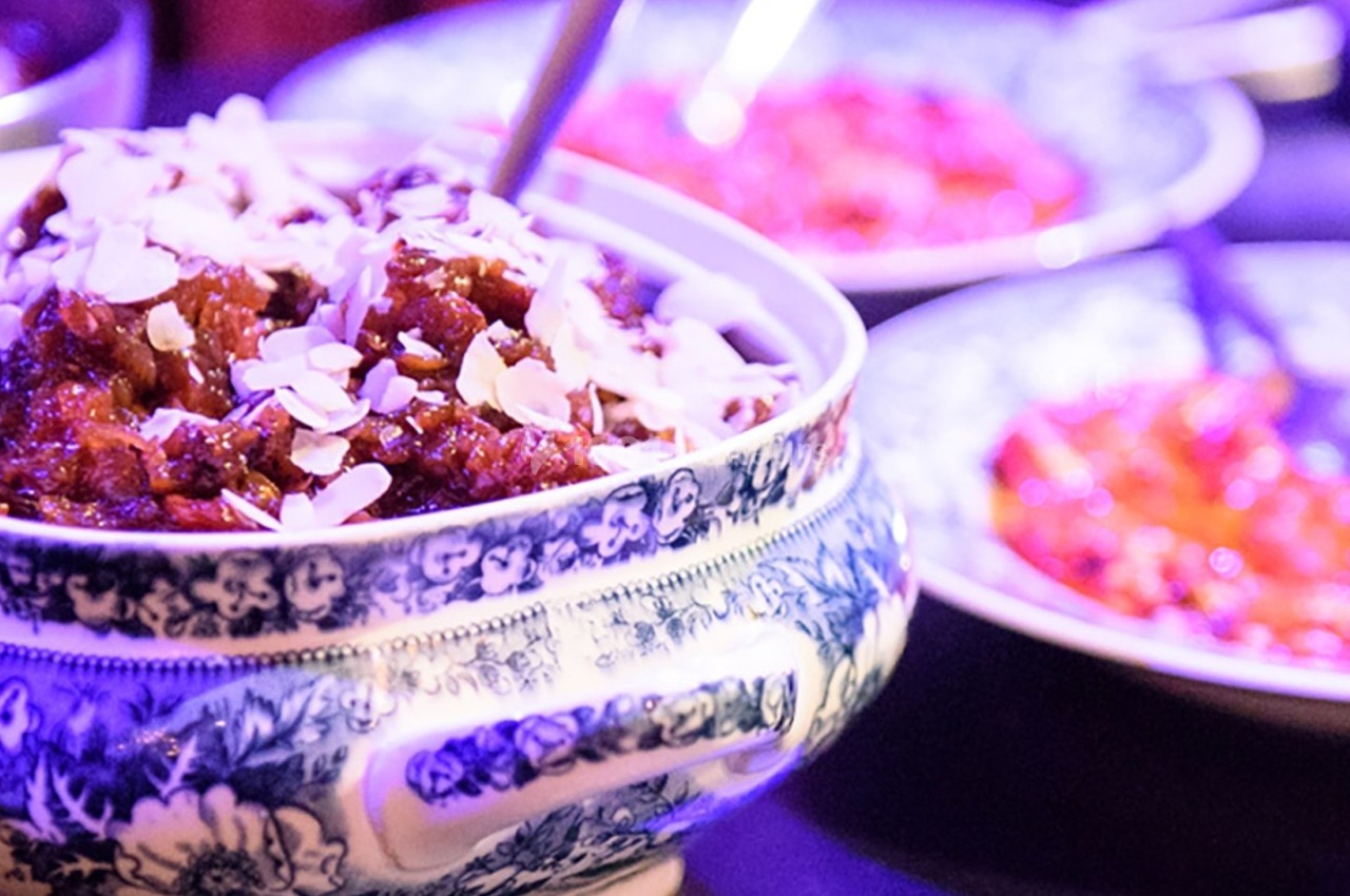 Plat en céramique décorée contenant un mets garni d'amandes effilées, entouré d'autres assiettes colorées.