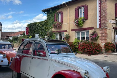 Miniature Location salle Condeissiat (Ain) - Restaurant Rolande #6 Une voiture Citroën 2CV rouge et blanche est garée devant un restaurant à façade fleurie dans un village.