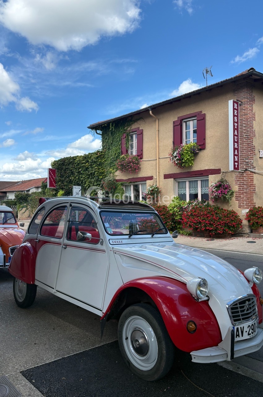 Voiture ancienne rouge et blanche stationnée devant un restaurant avec façade en briques et volets rouges.
