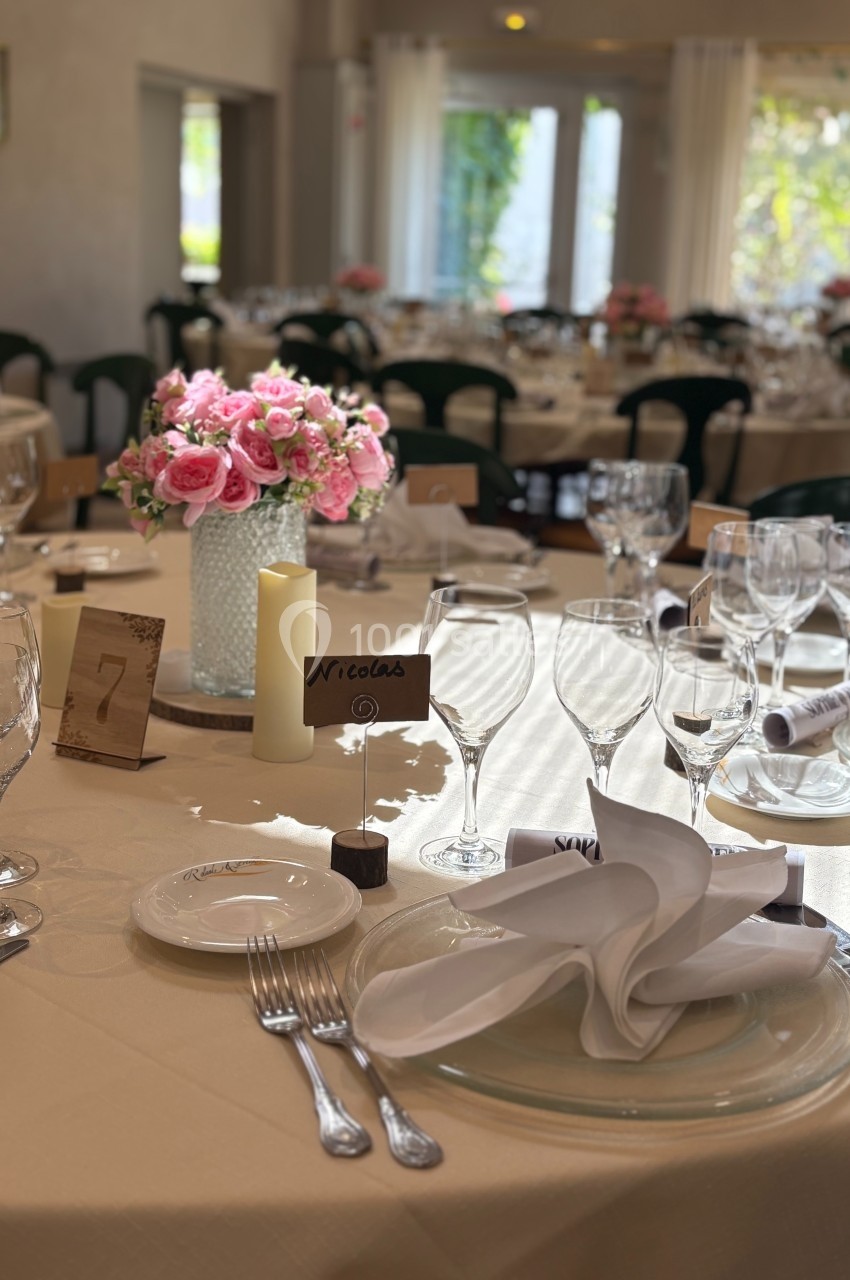 Table élégamment dressée avec vaisselle, serviettes pliées, bouquet de fleurs roses et carte de placement.