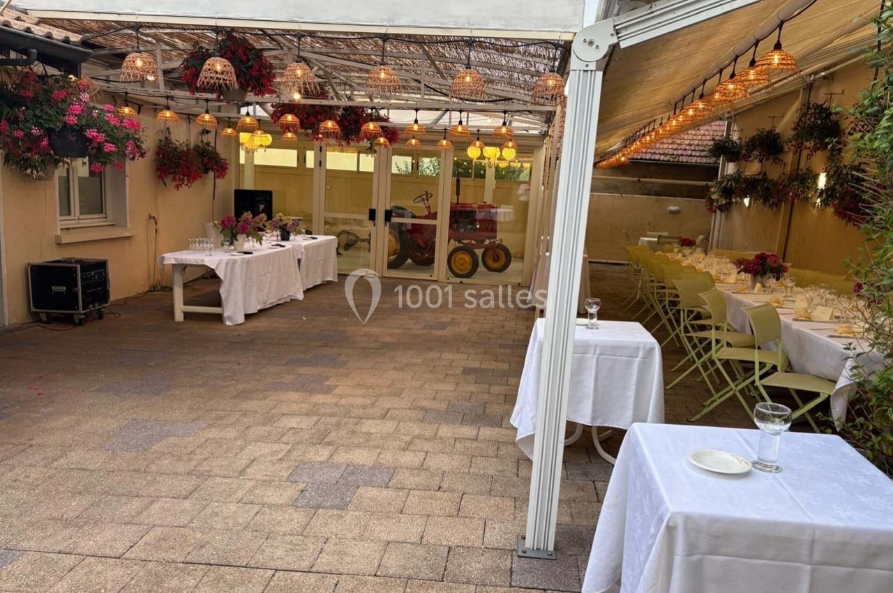 Espace extérieur couvert avec tables dressées, chaises alignées et décorations florales suspendues.