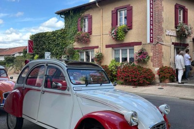 Miniature Location salle Condeissiat (Ain) - Restaurant Rolande #24 Une voiture Citroën 2CV rouge et blanche est garée devant un restaurant à façade fleurie dans un village.