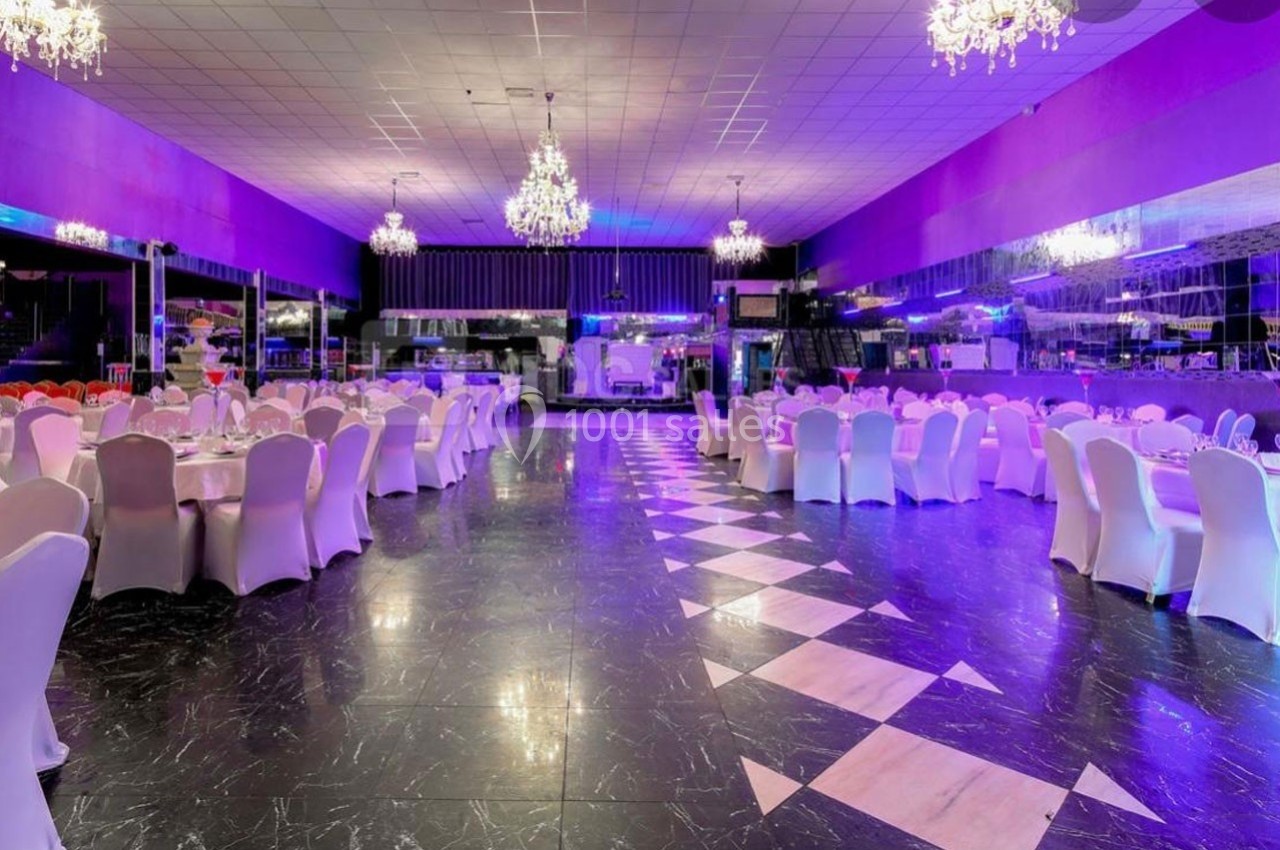 Salle de réception spacieuse avec tables rondes dressées, chaises blanches et lustres suspendus, éclairage violet.