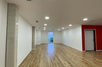 Salle vide avec parquet en bois clair, murs blancs, éclairage encastré au plafond et grande baie vitrée donnant sur l…