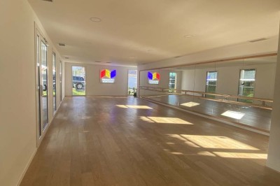 Salle vide avec parquet en bois clair, murs blancs, éclairage encastré au plafond et grande baie vitrée donnant sur l…