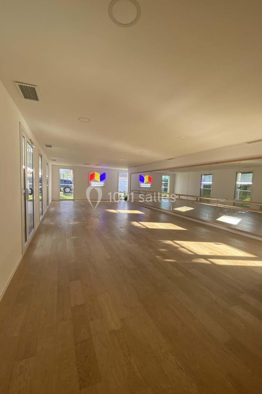Salle lumineuse avec parquet en bois clair, miroirs muraux et fenêtres laissant entrer la lumière naturelle.