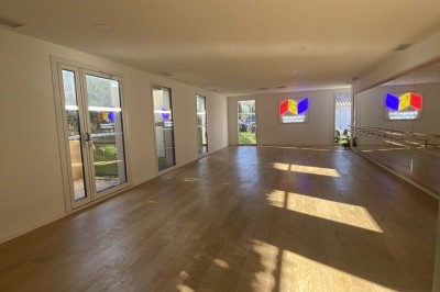 Salle vide avec parquet en bois clair, murs blancs, éclairage encastré au plafond et grande baie vitrée donnant sur l…