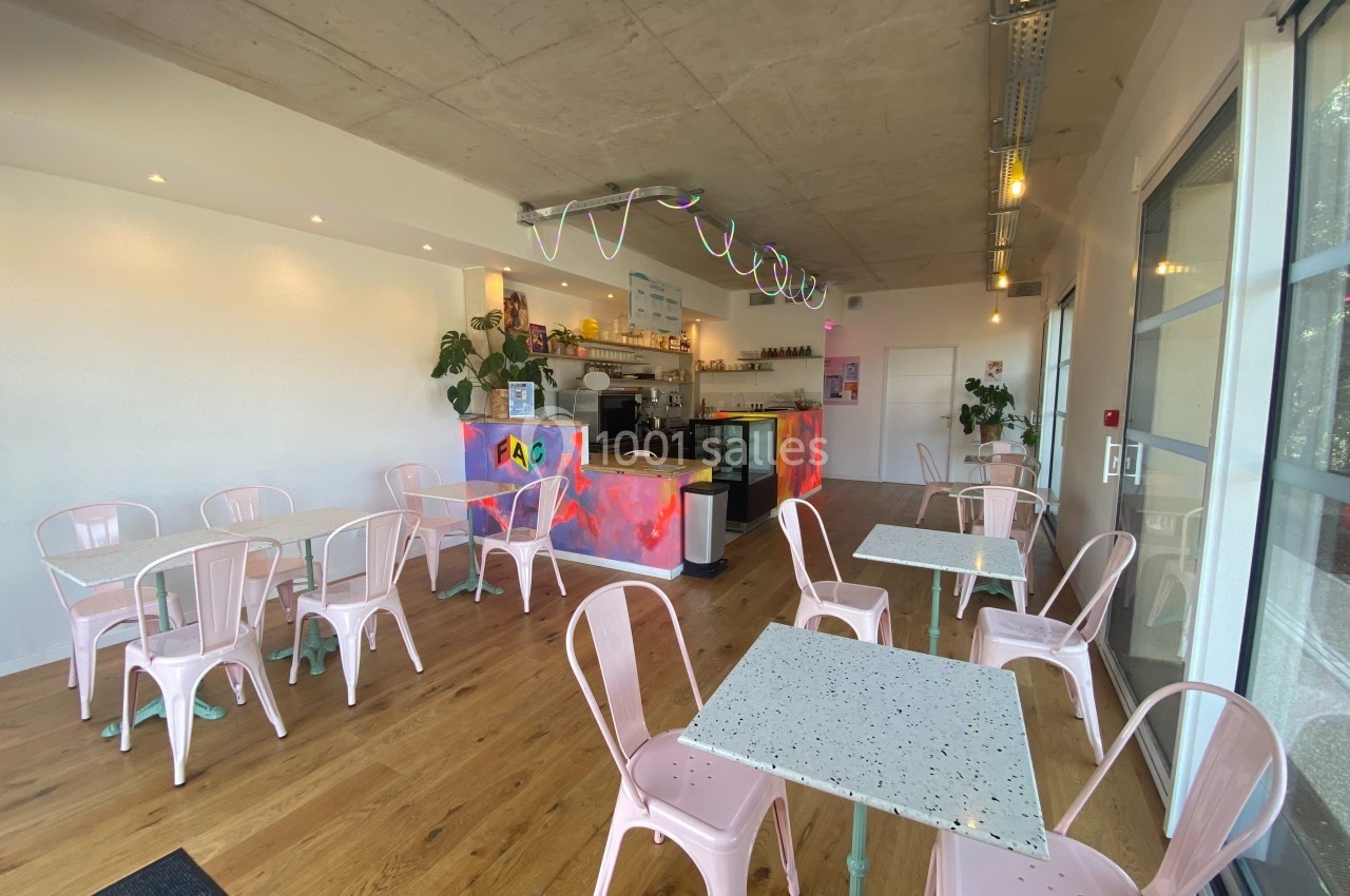 Salle lumineuse d'un café moderne avec des chaises roses, tables en terrazzo et comptoir coloré.
