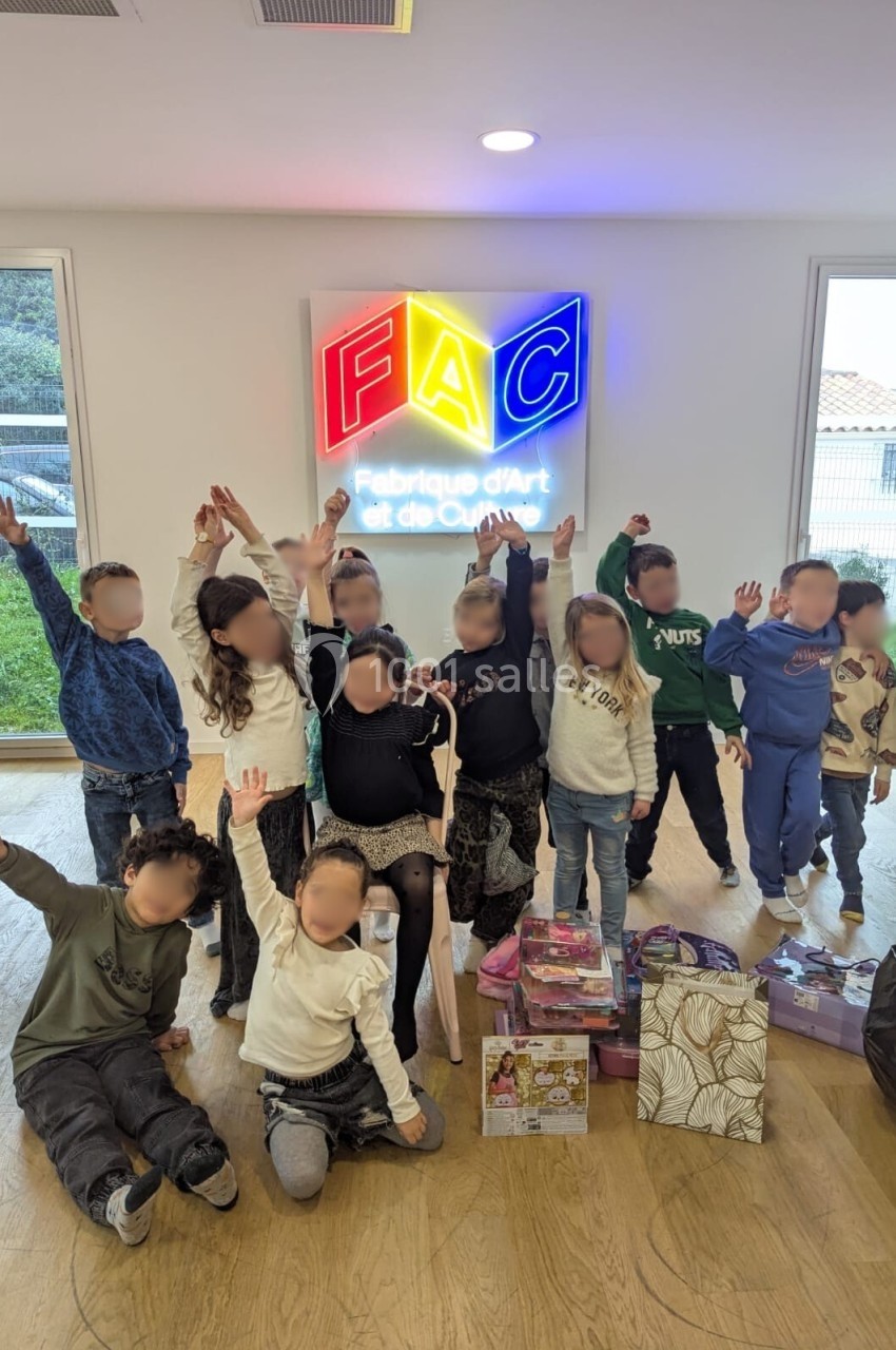 Des enfants souriants lèvent les bras dans une salle lumineuse devant un logo coloré ’FAC’.