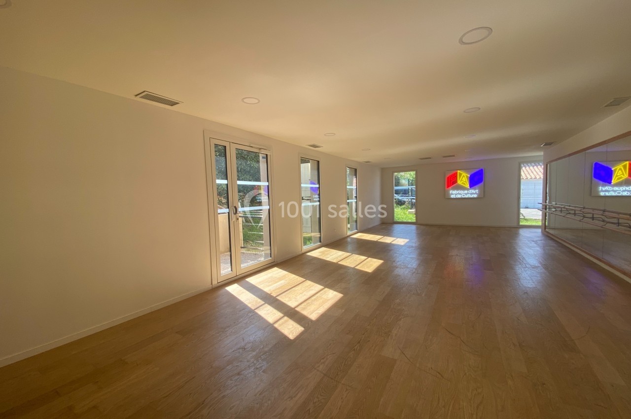 Salle lumineuse avec parquet, grandes fenêtres laissant entrer la lumière naturelle et miroirs sur un mur.
