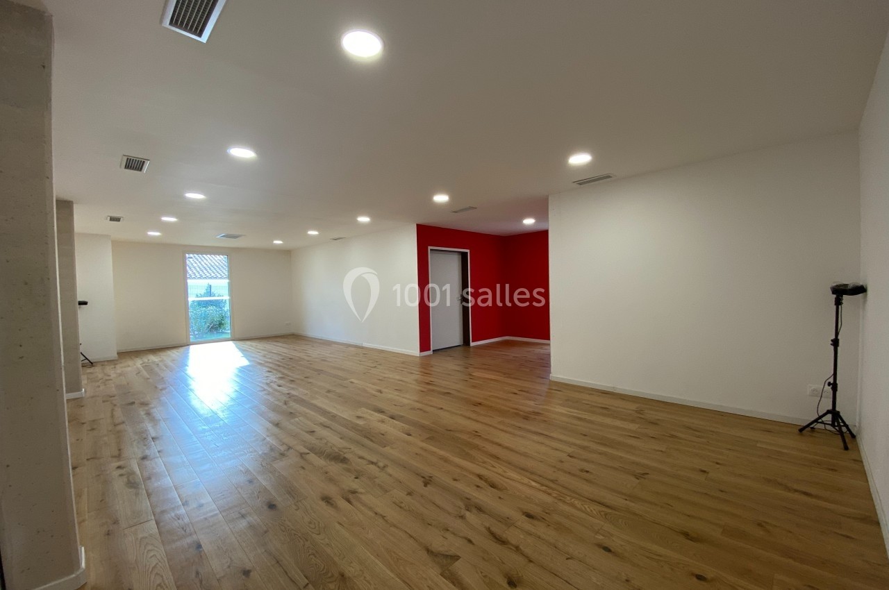 Salle spacieuse avec parquet en bois clair, murs blancs et rouges, éclairage encastré et grande porte vitrée.