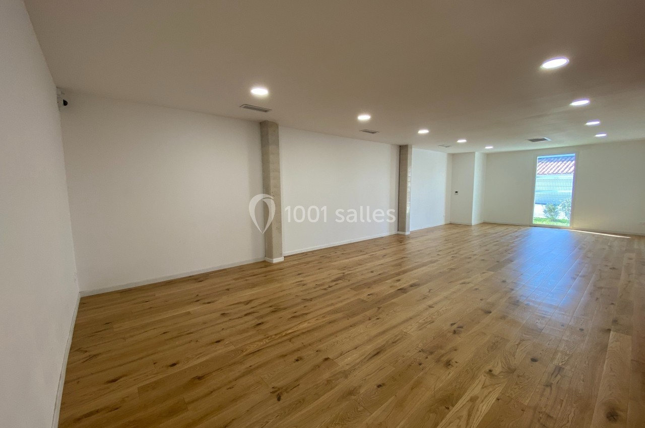 Salle vide avec parquet en bois clair, murs blancs, éclairage encastré au plafond et grande baie vitrée donnant sur l…