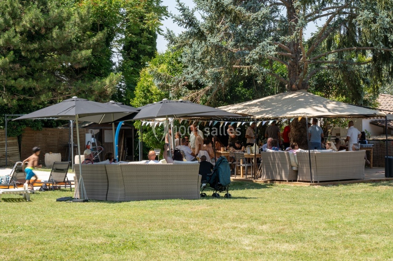 Groupe de personnes réunies dans un jardin avec des parasols, des canapés et une piscine en arrière-plan.