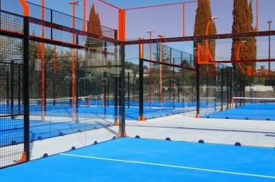 Miniature Location salle Simiane-Collongue (Bouches-du-Rhône) - Restaurant du Cercle #12 Terrain de padel extérieur avec sol bleu, clôtures en verre et grillage, entouré d'arbres et de filets orange.