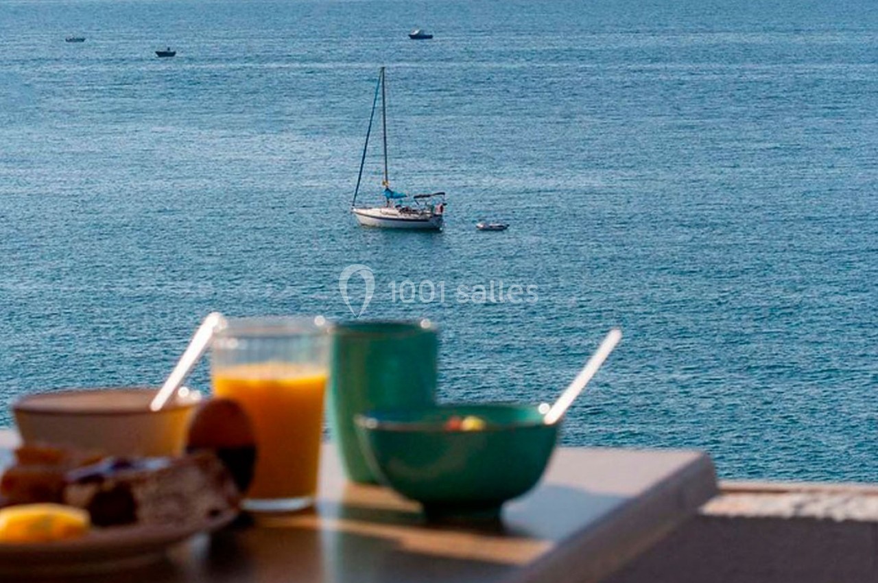 Petit-déjeuner avec vue sur la mer, un voilier et des bateaux au loin sur l'eau calme.
