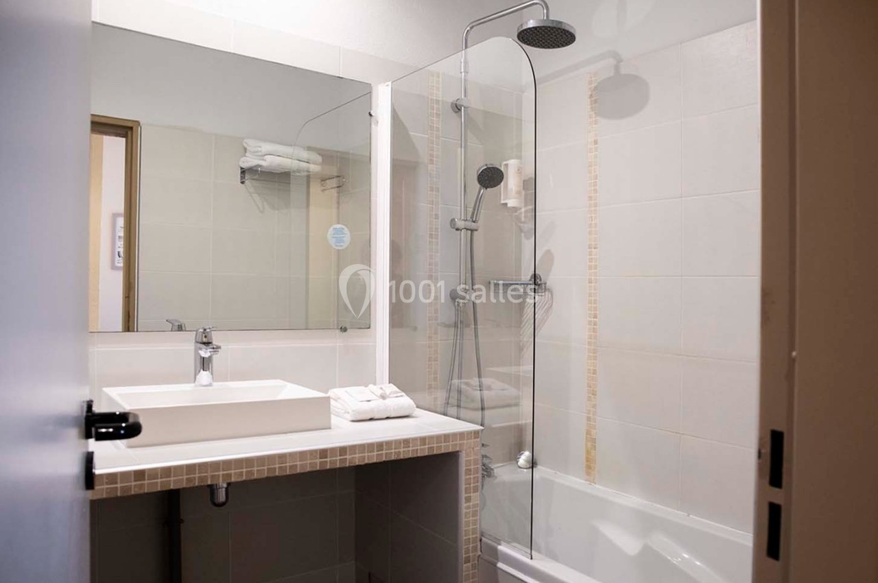 Salle de bain moderne avec lavabo, miroir, baignoire équipée d'une paroi vitrée et douchette murale.