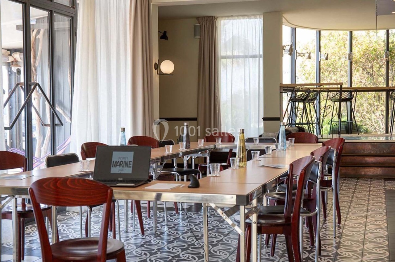 Salle de réunion lumineuse avec une grande table, chaises en bois, bouteilles d'eau et matériel de présentation.