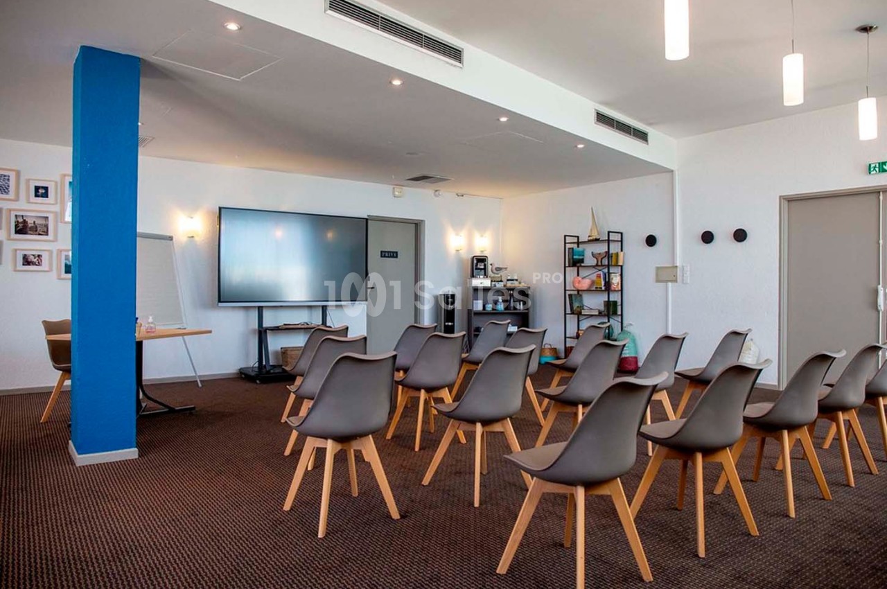 Salle de réunion équipée avec chaises disposées face à un écran, un paperboard et une étagère en arrière-plan.