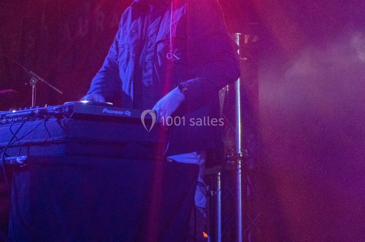 Un DJ mixant sur une table de mixage, éclairé par des lumières violettes dans une ambiance de concert.