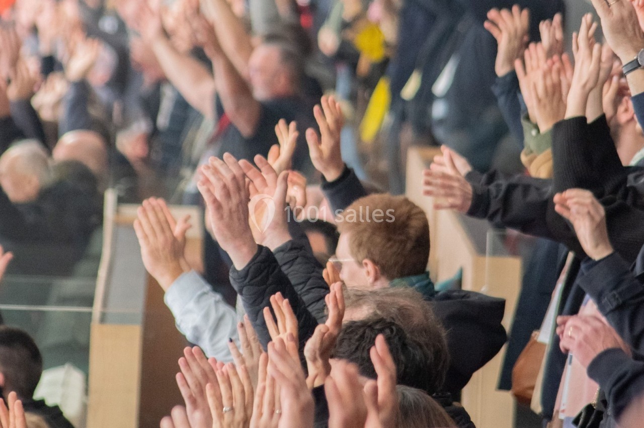 Des spectateurs applaudissent en levant les bras dans une tribune bondée lors d'un événement.