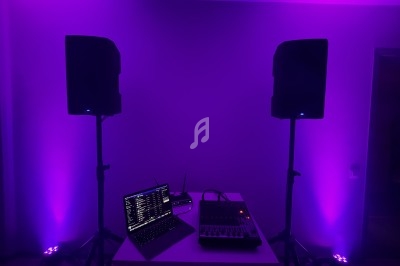 Deux enceintes sur pied, un ordinateur portable et une table de mixage éclairés par une lumière violette.