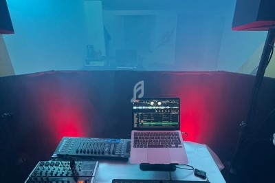 Table de mixage avec contrôleurs DJ, ordinateur portable et éclairage coloré dans une ambiance de salle enfumée.