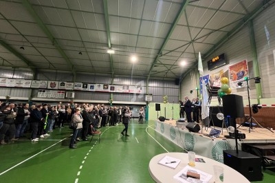 Un groupe de personnes assiste à une présentation sur une scène dans un gymnase décoré de ballons et de banderoles.