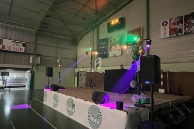 Scène éclairée avec des projecteurs colorés dans une salle de sport, équipée de haut-parleurs et décorée de ballons.
