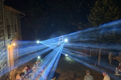 Dîner en plein air nocturne avec des invités assis à une longue table éclairée par des faisceaux lumineux.