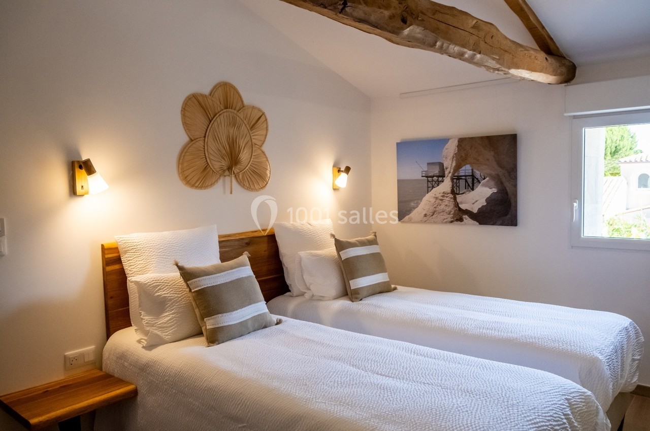 Deux lits simples avec linge blanc dans une chambre lumineuse, décorée avec des éléments naturels et un tableau mural.