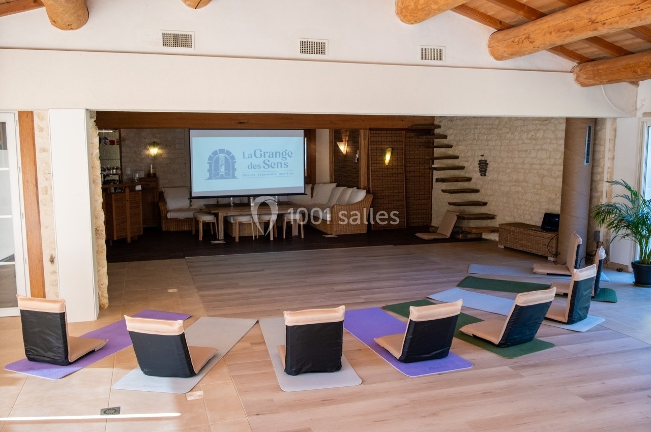 Salle lumineuse avec tapis de yoga et chaises de méditation disposés face à un écran de projection.