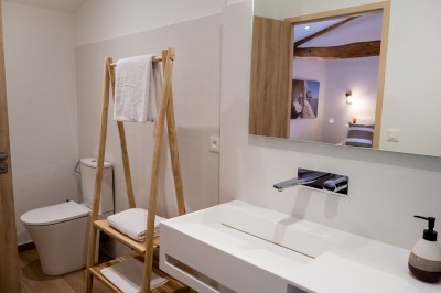 Salle de bain moderne avec lavabo blanc, miroir, porte-serviettes en bois et toilettes, éclairée par une lumière douce.