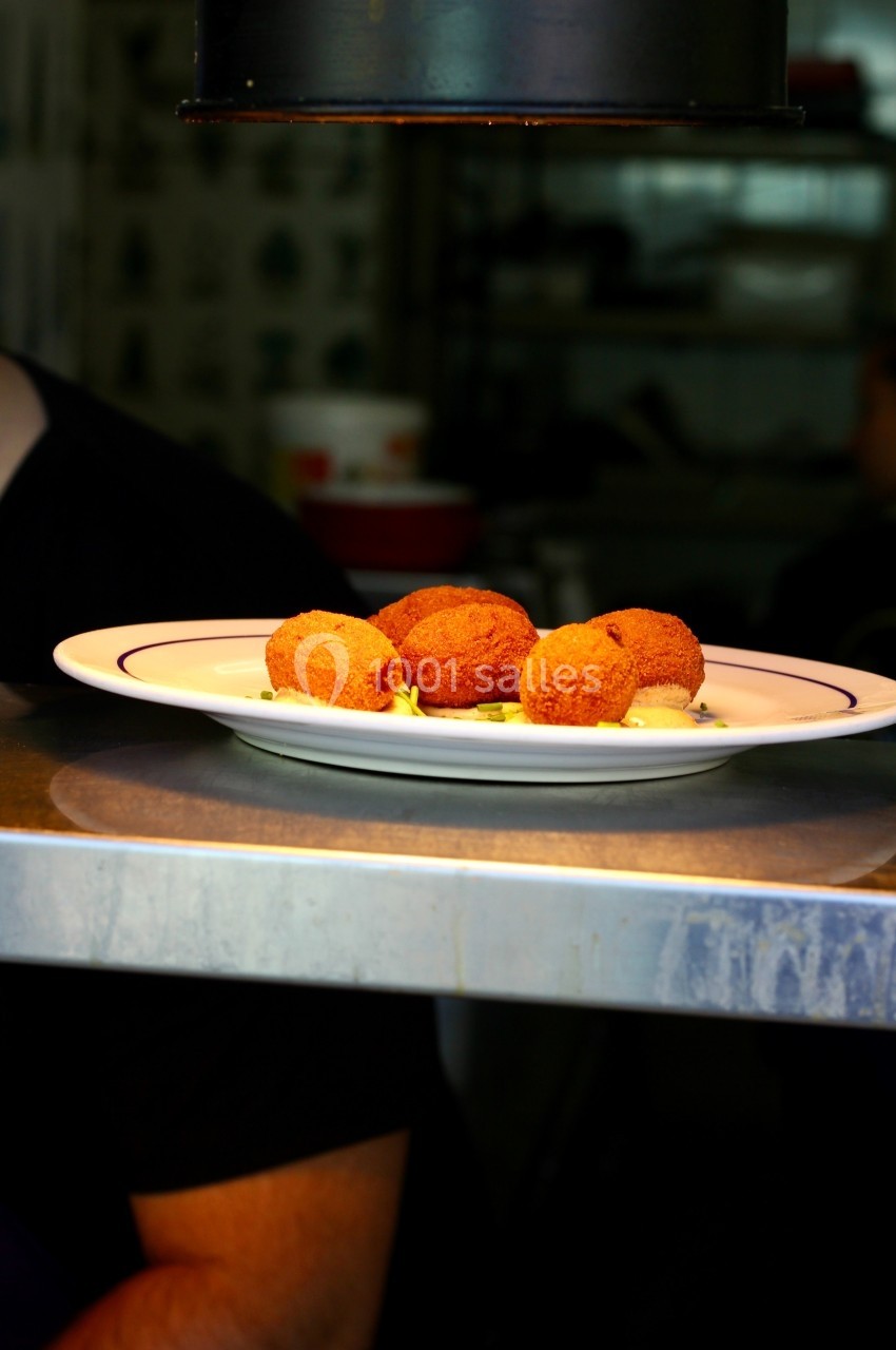 Assiette blanche contenant plusieurs croquettes dorées posée sur un comptoir en métal dans un environnement de cuisine.