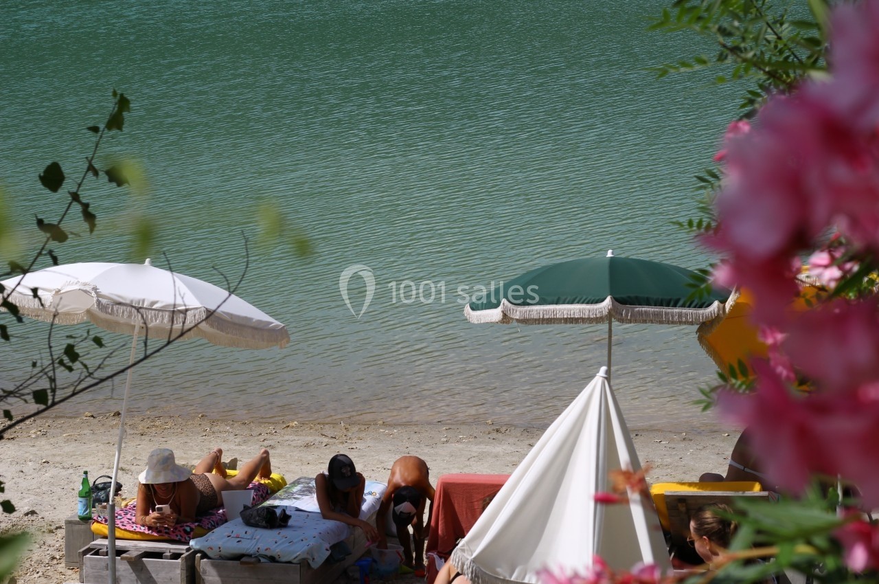 Personnes se relaxant sous des parasols au bord d'un lac entouré de végétation.