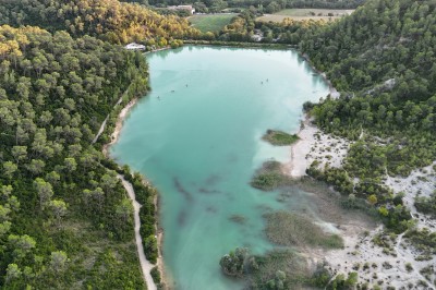 Vue aérienne d'un lac entouré de collines boisées sous un ciel dégagé au coucher du soleil.