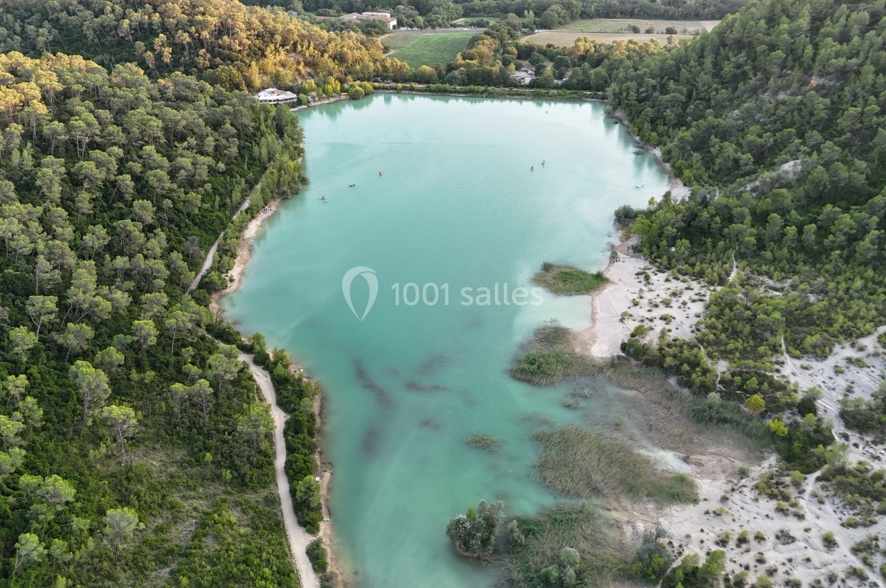 Vue aérienne d'un lac entouré de forêts et de végétation, avec des chemins et des zones sablonneuses sur les rives.
