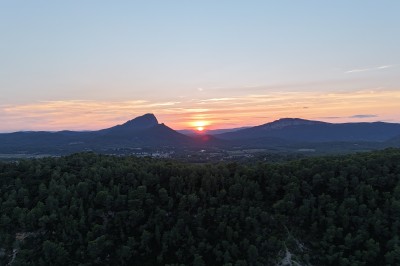 Vue aérienne d'un lac entouré de collines boisées sous un ciel dégagé au coucher du soleil.