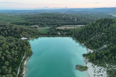 Vue aérienne d'un lac entouré de collines boisées sous un ciel dégagé au coucher du soleil.
