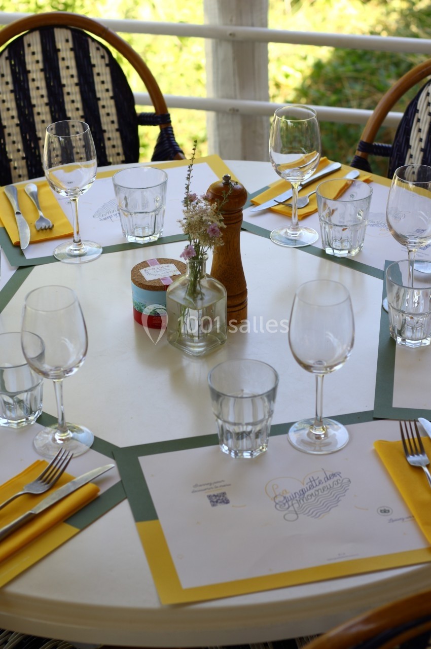 Table dressée en extérieur avec verres, couverts, serviettes jaunes et un centre de table floral.