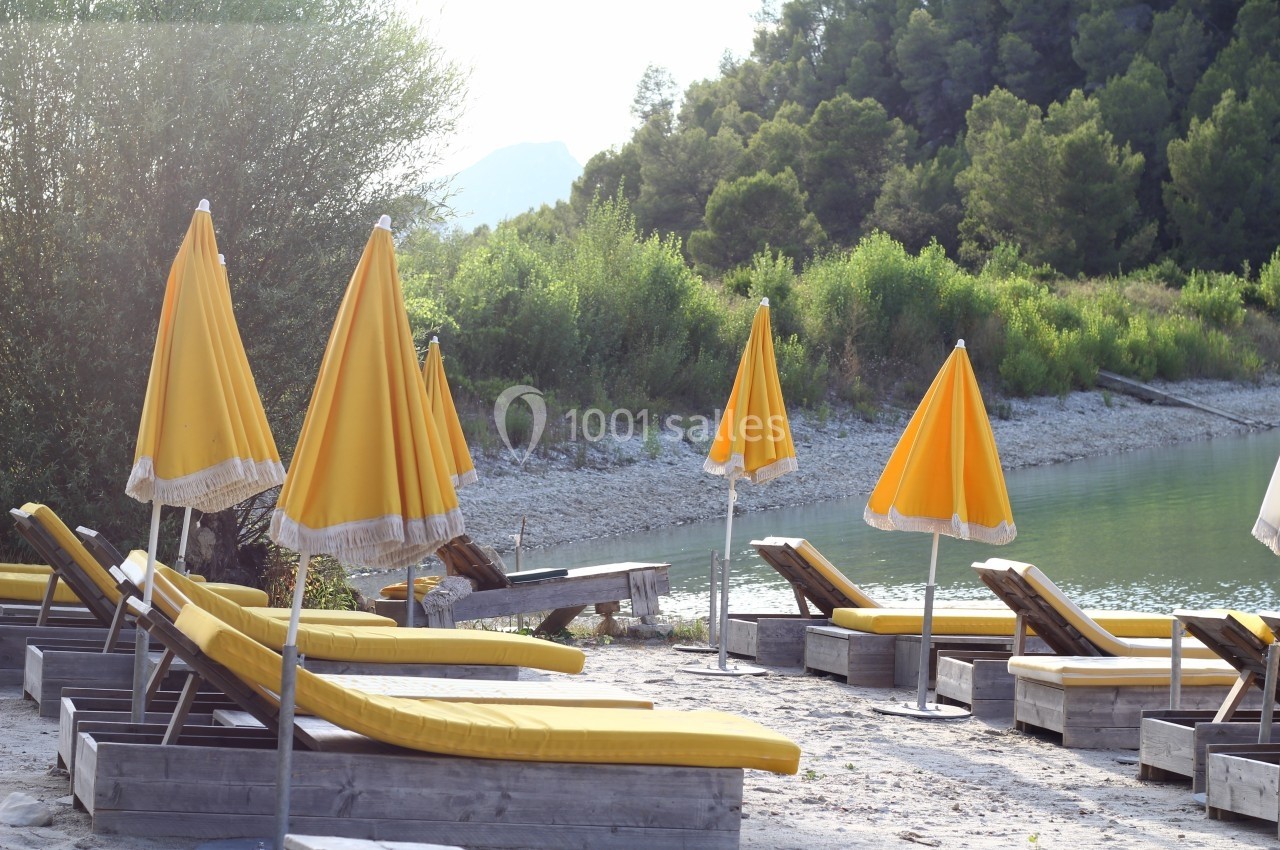 Chaises longues jaunes et parasols alignés sur une plage au bord d'un lac entouré de végétation.