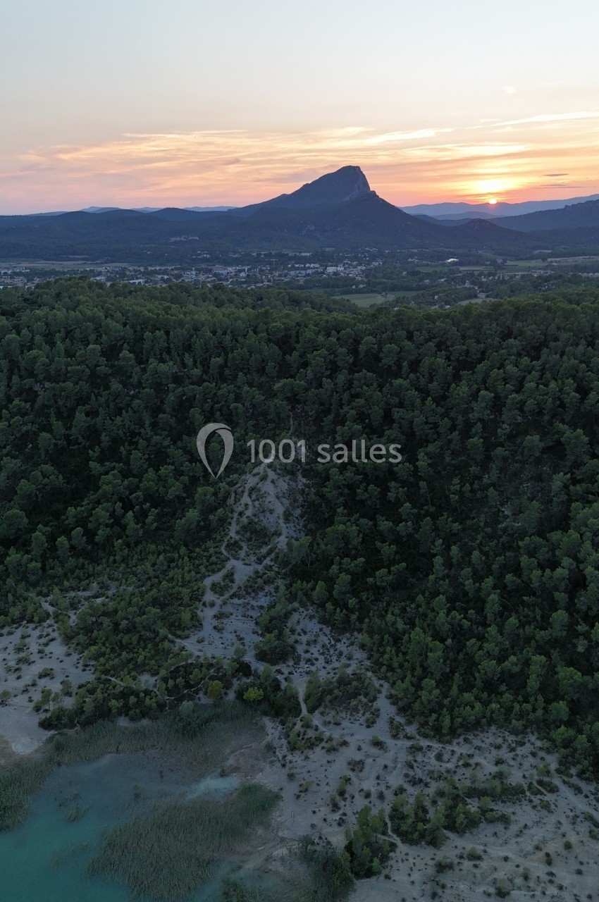 Vue aérienne d'un paysage naturel au coucher du soleil, avec une forêt, un lac et une montagne à l'horizon.