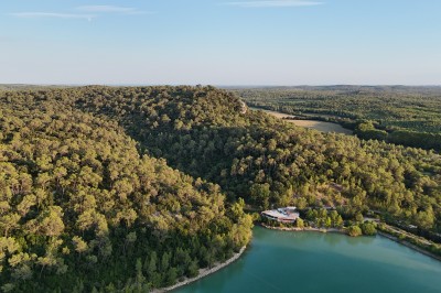 Vue aérienne d'un lac entouré de collines boisées sous un ciel dégagé au coucher du soleil.