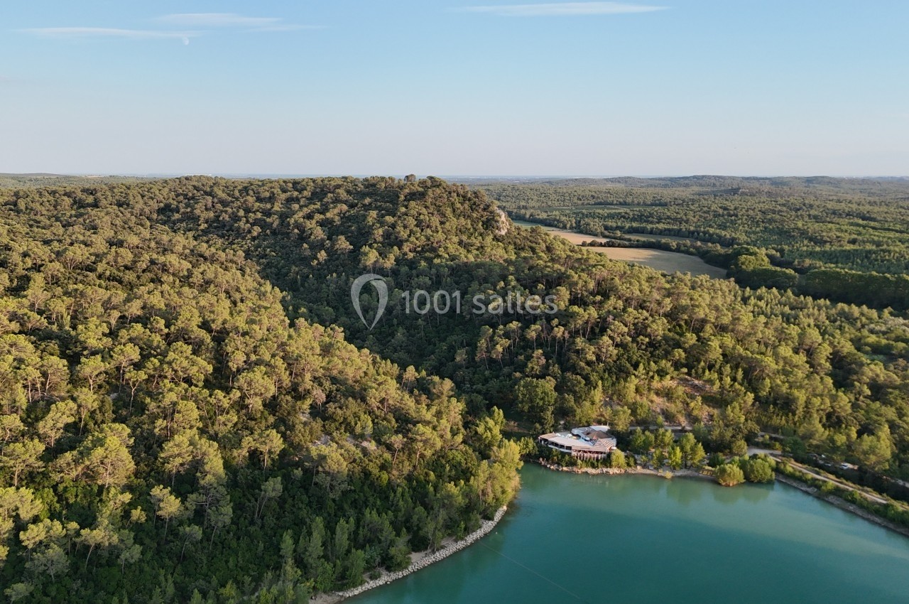 Vue aérienne d'une forêt dense bordant un lac aux eaux calmes, sous un ciel dégagé.