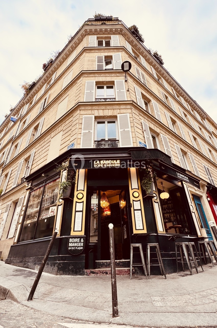 Façade d'un café d'angle parisien avec terrasse et enseigne ’La Bascule’, situé dans un immeuble haussmannien.